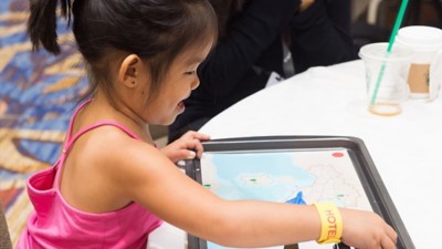 A child wearing a pink tank top interacting with a map on a tablet device