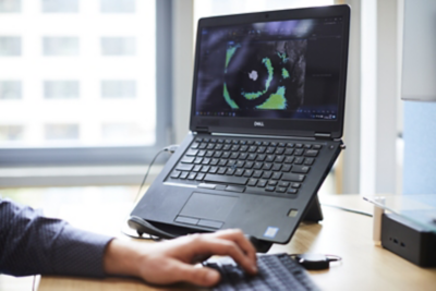 Hand op een computermuis naast een laptop met een geografische visualisatie op het scherm.